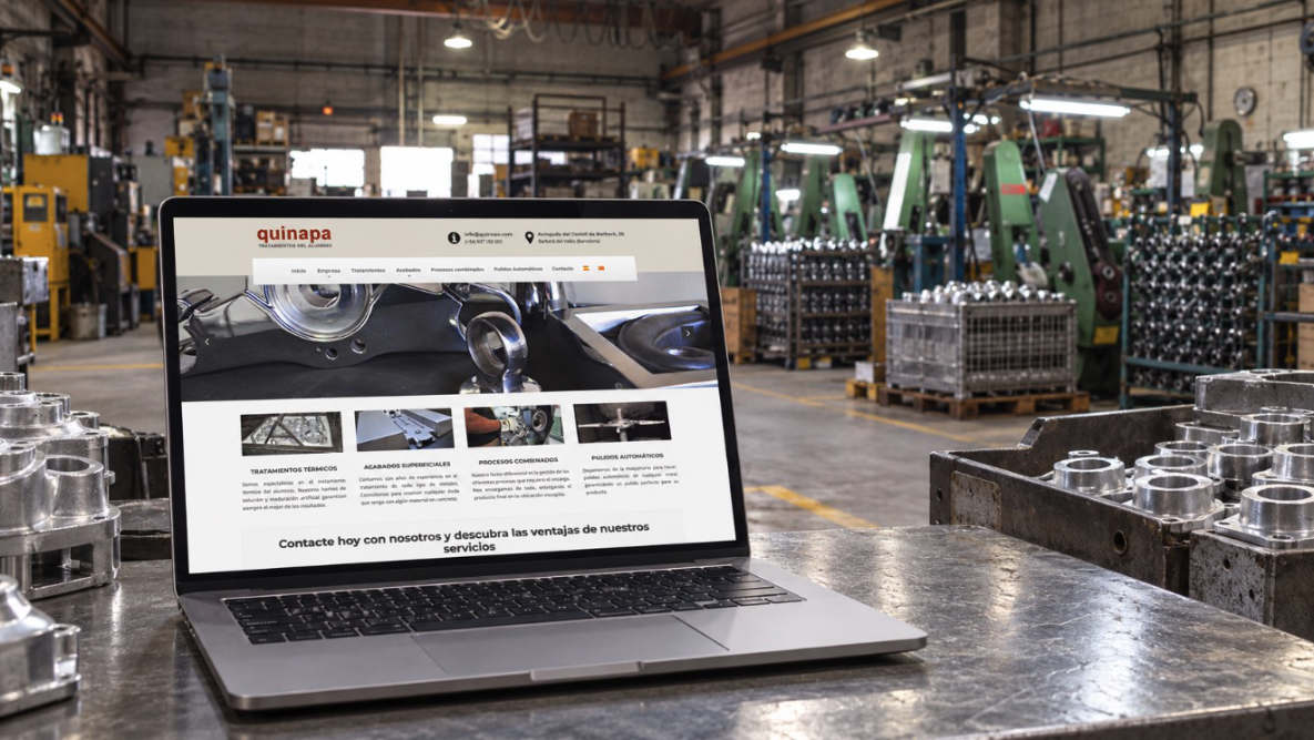 Diseño web de Quinapa en Barberà del Vallès Portátil sobre una mesa metálica mostrando la web de Quinapa, con maquinaria y piezas de aluminio al fondo